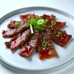Korean Beef Bulgogi served on a white plate. Thinly sliced beef is coated in a glossy sweet soy glaze, garnished with sesame seeds and chopped green onions