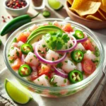 Classic Mexican Ceviche in a glass bowl, featuring chunks of fresh white fish, avocado slices, red onion, diced tomatoes, jalapeños, and cilantro, all dressed in fresh lime juice and garnished with lime wedges.