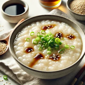 A close-up image of a warm bowl of congee with a creamy, slightly watery texture, drizzled with sesame soy dressing and garnished with chopped green onions.